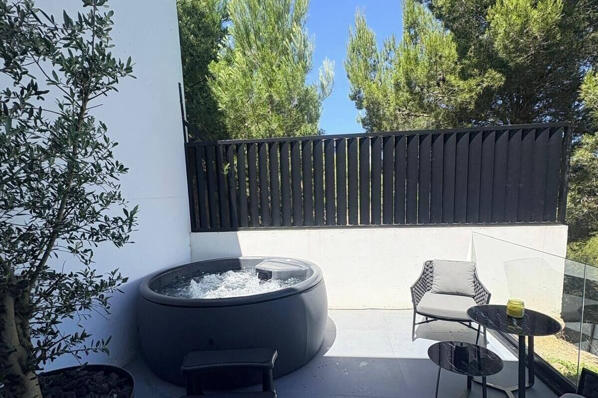 Un patio moderno al aire libre con un pozo de fuego circular, asientos y vistas a árboles altos.