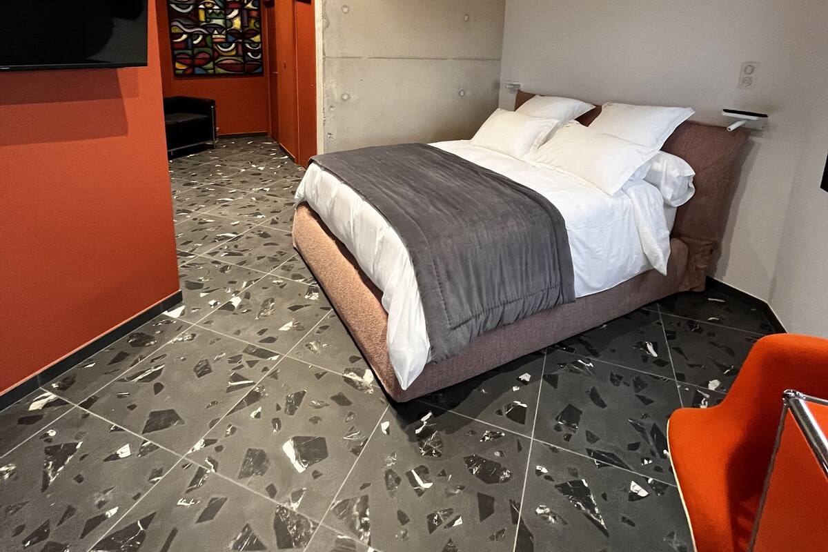 Una habitación de hotel moderna con cama, televisor, pared roja y suelo estampado.