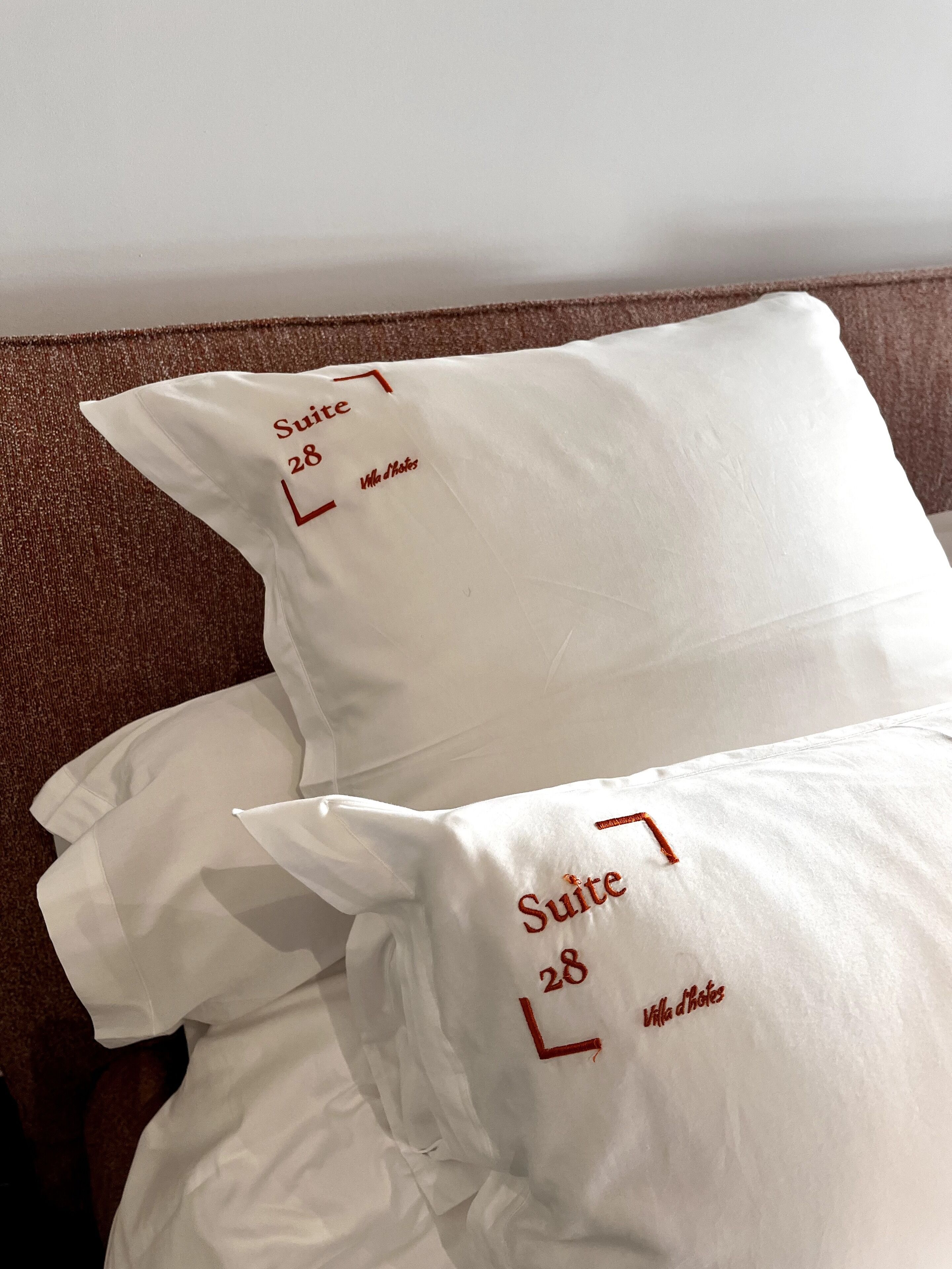 Two white pillows with embroidered text "Suite 28" and "Villa d'Hotel" on a brown textured surface.