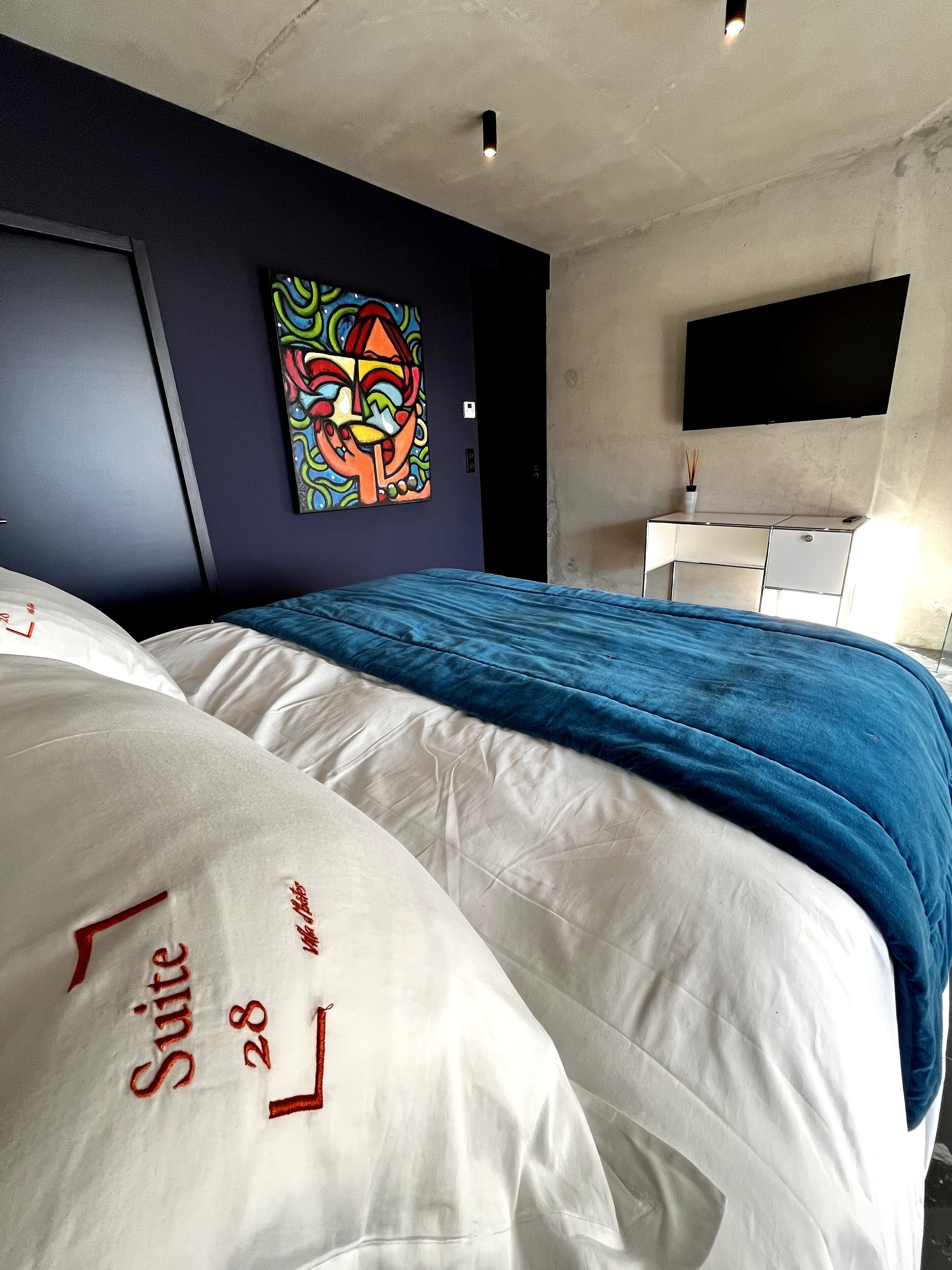 A modern bedroom with a bed, a painting, a TV, and a desk.