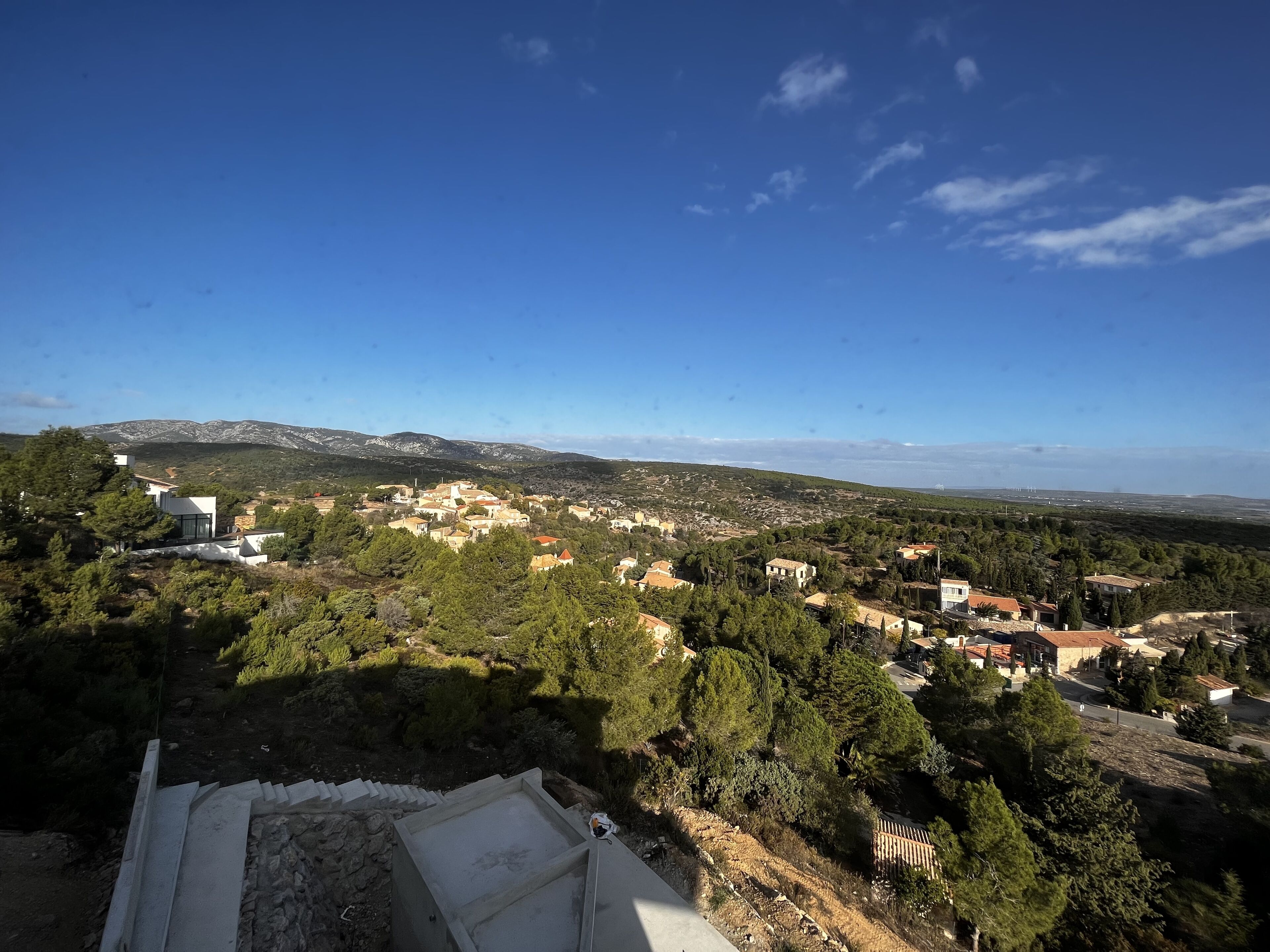 Een panoramisch uitzicht op een kustplaatsje, met gebouwen omgeven door groen en bergen op de achtergrond.