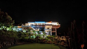 A modern multi-story building with a well-lit exterior, surrounded by landscaped gardens and a golf course. - SUITE 28 (Treilles)