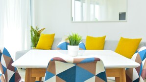 Un comedor con una mesa blanca, sillas de colores con estampado y cojines amarillos, además de una planta en maceta.