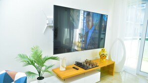 Una sala de estar moderna con un televisor de pantalla plana montado en la pared, una mesa de centro de madera con un juego de ajedrez, una planta en maceta y un jarrón decorativo.