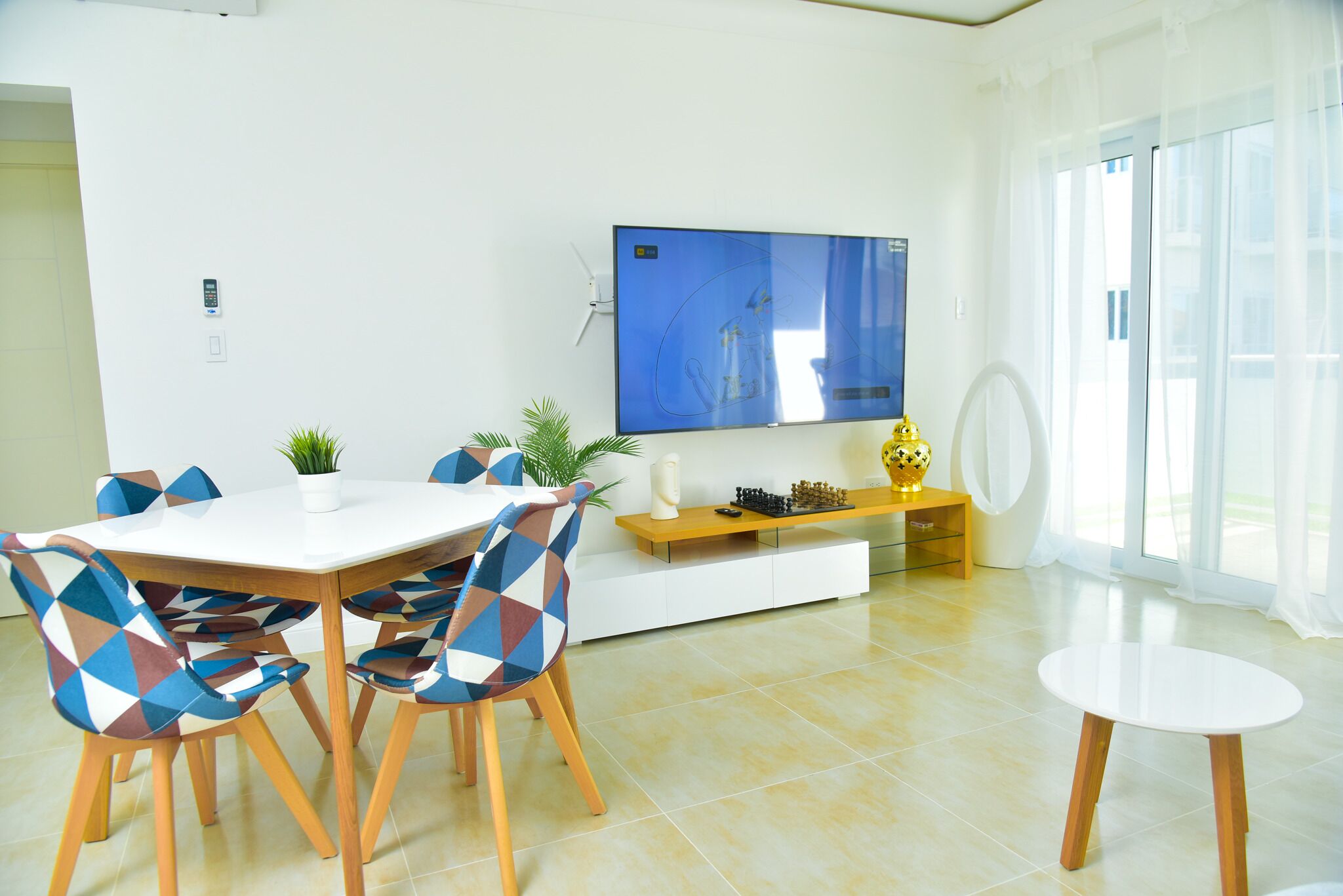 Un espace repas moderne avec une table blanche, des chaises colorées, un téléviseur à écran plat et une petite table ronde.
