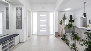 Une cuisine moderne avec des meubles blancs, un luminaire suspendu noir et un saladier de fruits posé sur le plan de travail.