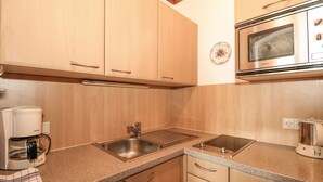 Una cocina con gabinetes de madera, un lavamanos de acero inoxidable, microondas integrado y cafetera.