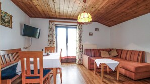 Una sala de estar acogedora con techo de madera, un sofá, un televisor montado en la pared y una mesa de comedor con sillas.