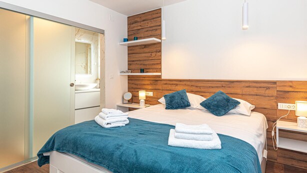 Une chambre moderne avec un lit, des tables de chevet, un miroir et une tête de lit en bois.