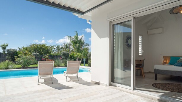 Een modern terras buiten met een zwembad, twee lounge fauteuils en een glazen schuifdeur naar een slaapkamer.