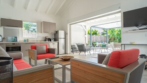 Een moderne keuken met een koelkast, fornuis en spoelbak. Er is een zithoek met een tafel en stoelen. De kamer heeft een groot raam en een plafondventilator.