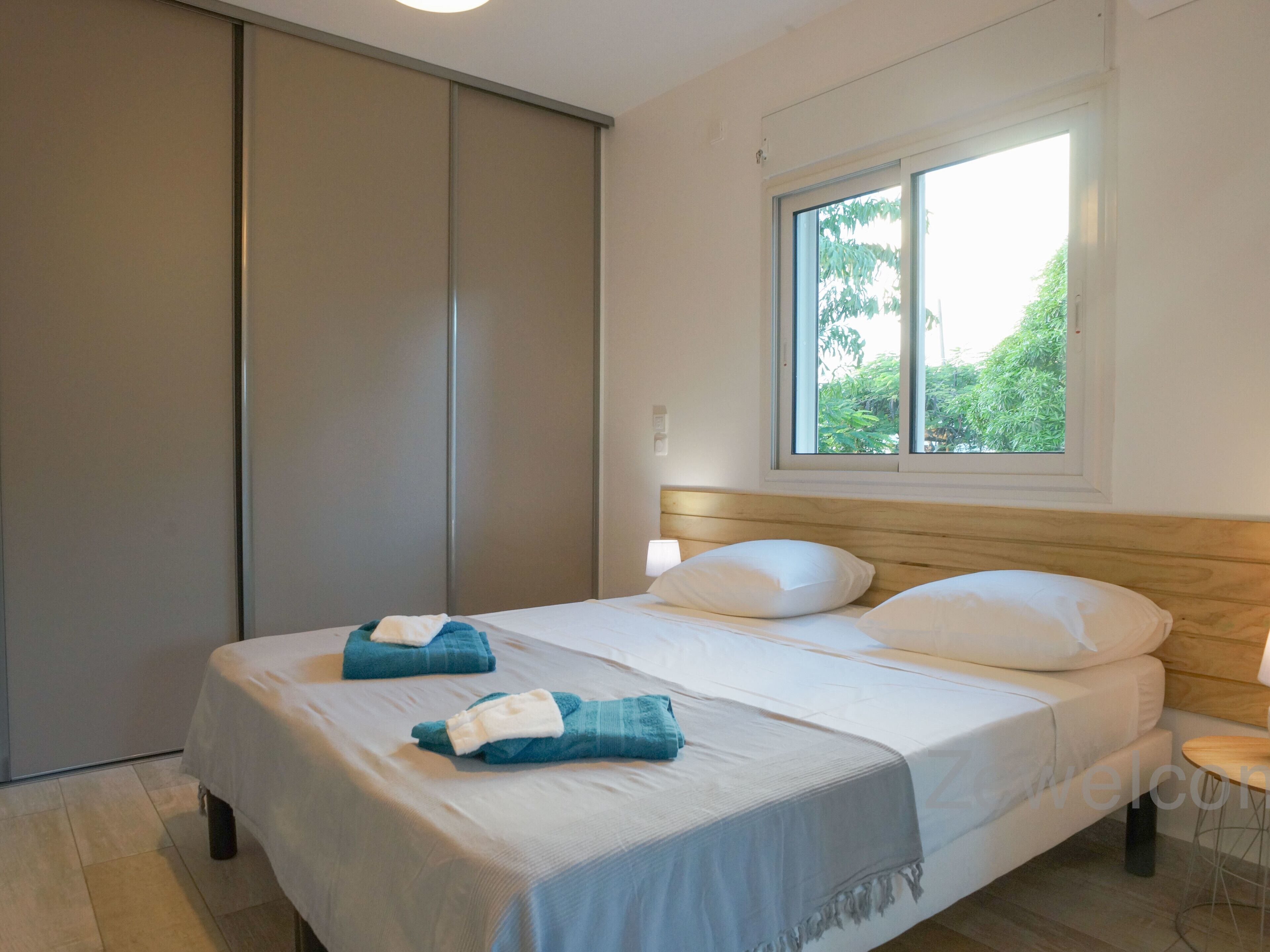 Ein modernes Schlafzimmer mit einem großen Bett, einem Holzkopfstück, einem Fenster mit Blick auf Grünflächen und einer Schiebetür.