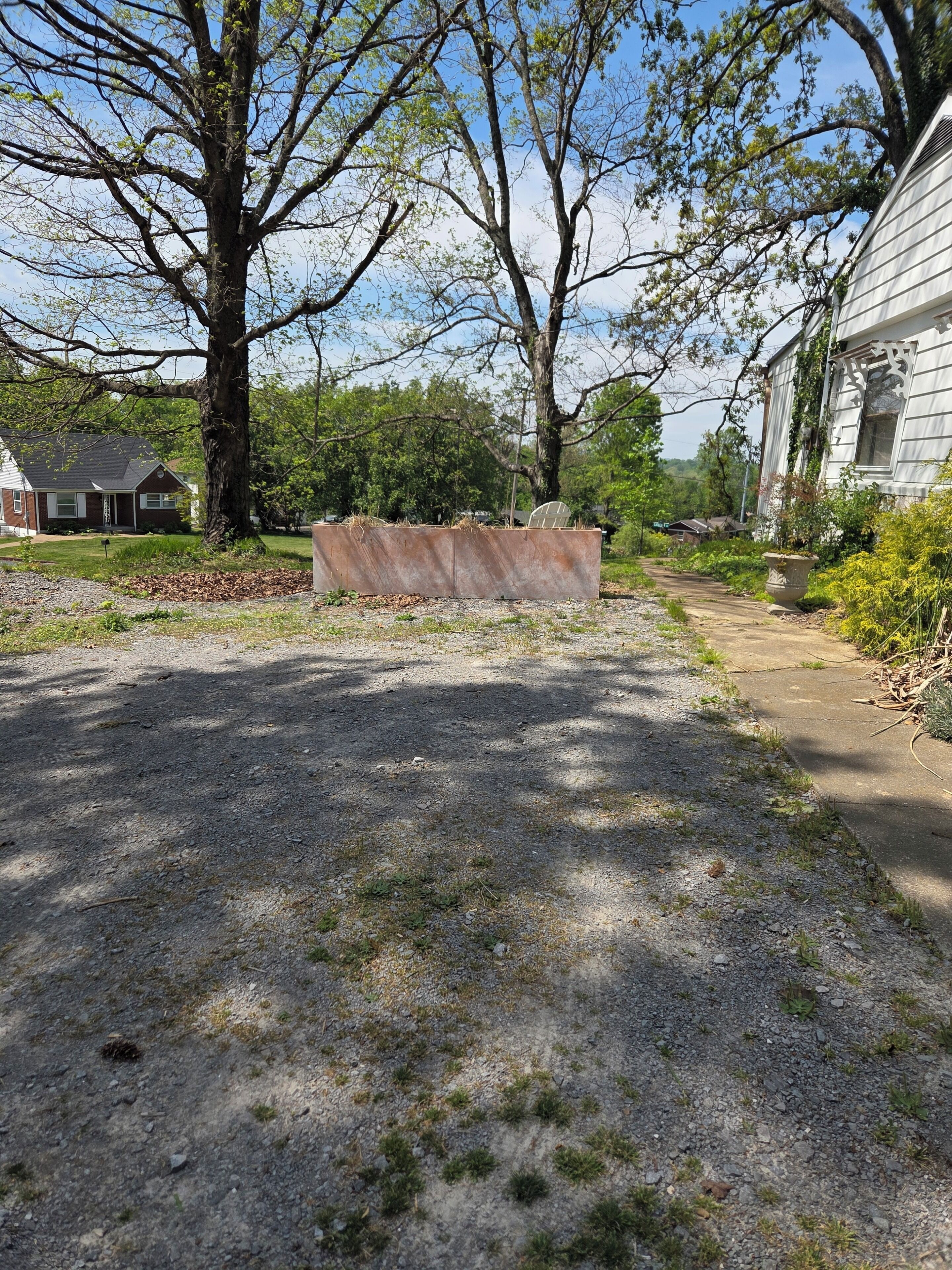 A gravel driveway leading to a house with a large tree in the foreground.