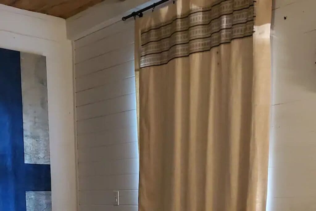 Een kamer met witte paneelwanden, een beige gordijn en een zichtbare lichtschakelaar.