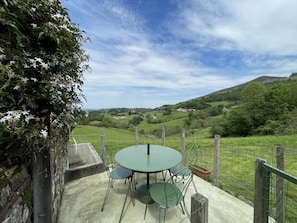A round table with four chairs, a concrete floor, and a view of a green landscape with hills and a house in the distance. - BELAZKABIETA - ESPELETTE (ESPELETTE)
