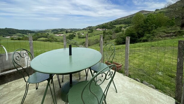 A round table with four chairs, a metal fence, and a view of rolling hills and distant houses. - BELAZKABIETA - ESPELETTE (ESPELETTE)