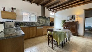 A spacious kitchen with wooden cabinets, a marble countertop, and a dining area with a table and chairs. - BELAZKABIETA - ESPELETTE (ESPELETTE)