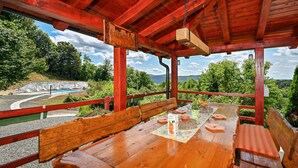 Una terraza de madera con una mesa dispuesta para comer, con vista a una piscina y abundante vegetación.