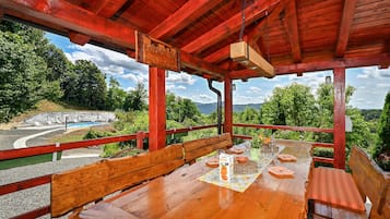 A wooden deck with a table set for dining, overlooking a pool and lush greenery.