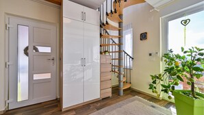 Un interior moderno con una escalera de madera, armarios blancos y una planta verde junto a una ventana.
