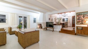Un amplio salón con mobiliario de mimbre, un televisor y una chimenea.