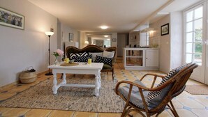 A cozy living room with a sofa, a dining table, and wicker chairs. A kitchen area is visible in the background. - GURE GOSTUAN - ITXASSOU (ITXASSOU)