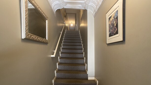 A staircase with a carpeted floor, white walls, and a framed mirror on the left.