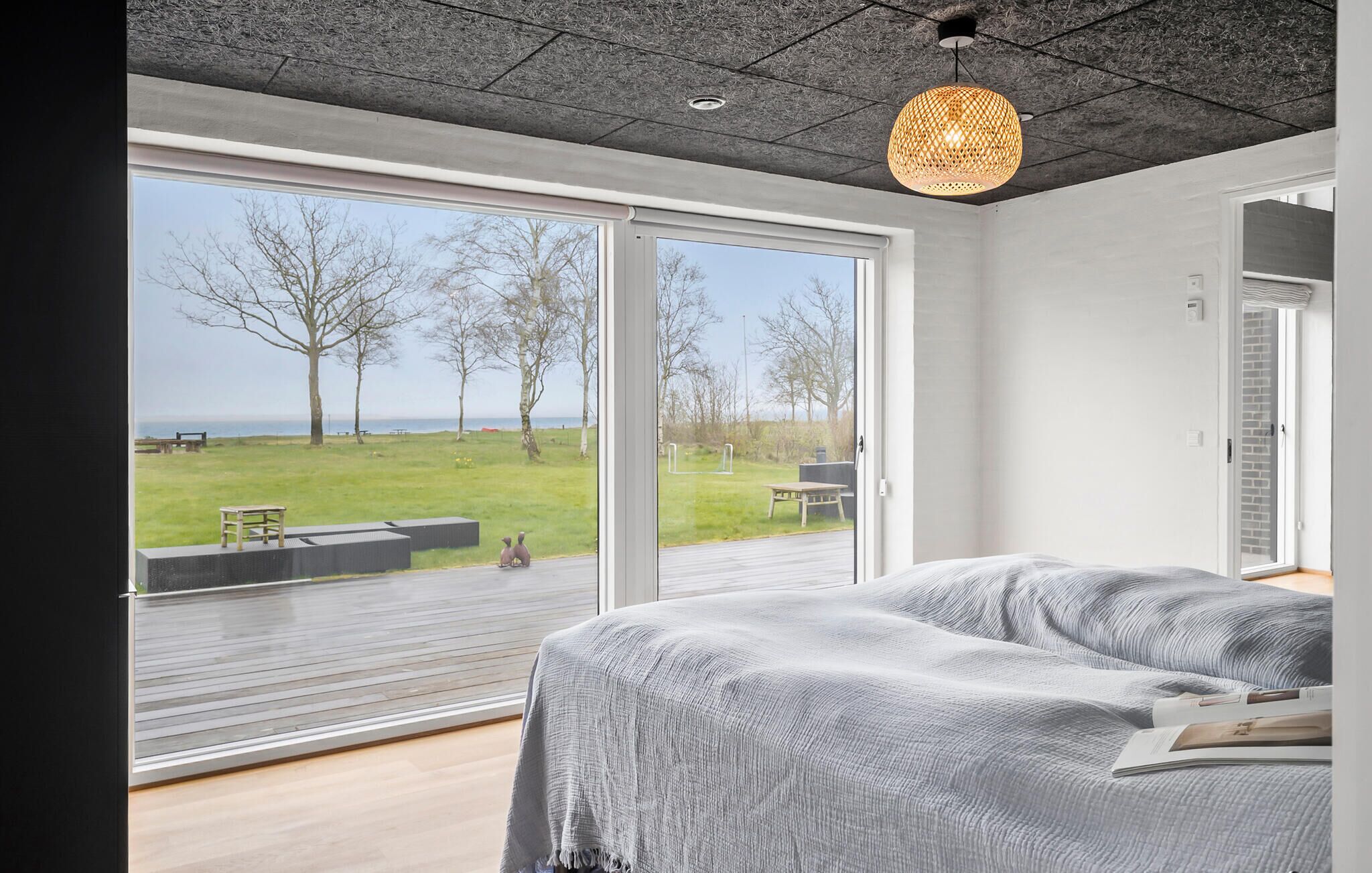 Une chambre dotée d’une grande porte-fenêtre coulissante qui donne sur un espace extérieur avec une pelouse et des arbres.