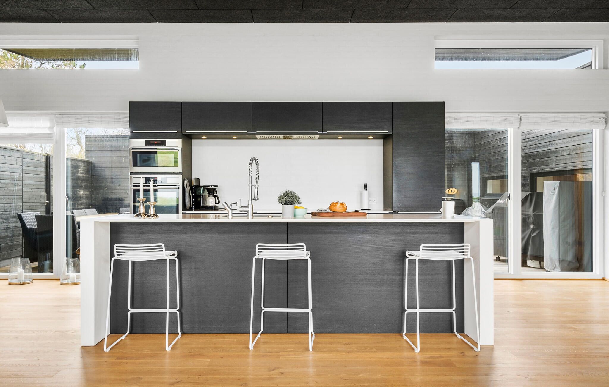 Una cocina moderna con una isla central, taburetes de bar y vistas al exterior.