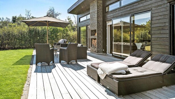 Eine Terrasse im Freien mit Korbmöbeln und einem Grill, mit Blick auf einen üppigen Garten.
