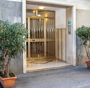 Entrada d'un edifici amb una porta d'ascensor de vidre, plantes en testos i un indicador amb el número del pis.