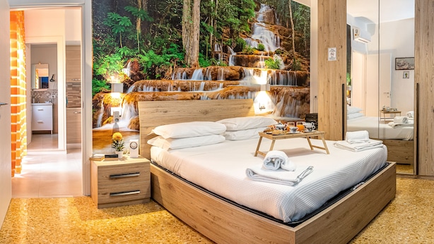 Une chambre avec un grand lit, une tête de lit en bois, des tables de chevet, une commode, un miroir et une fresque murale représentant une cascade.