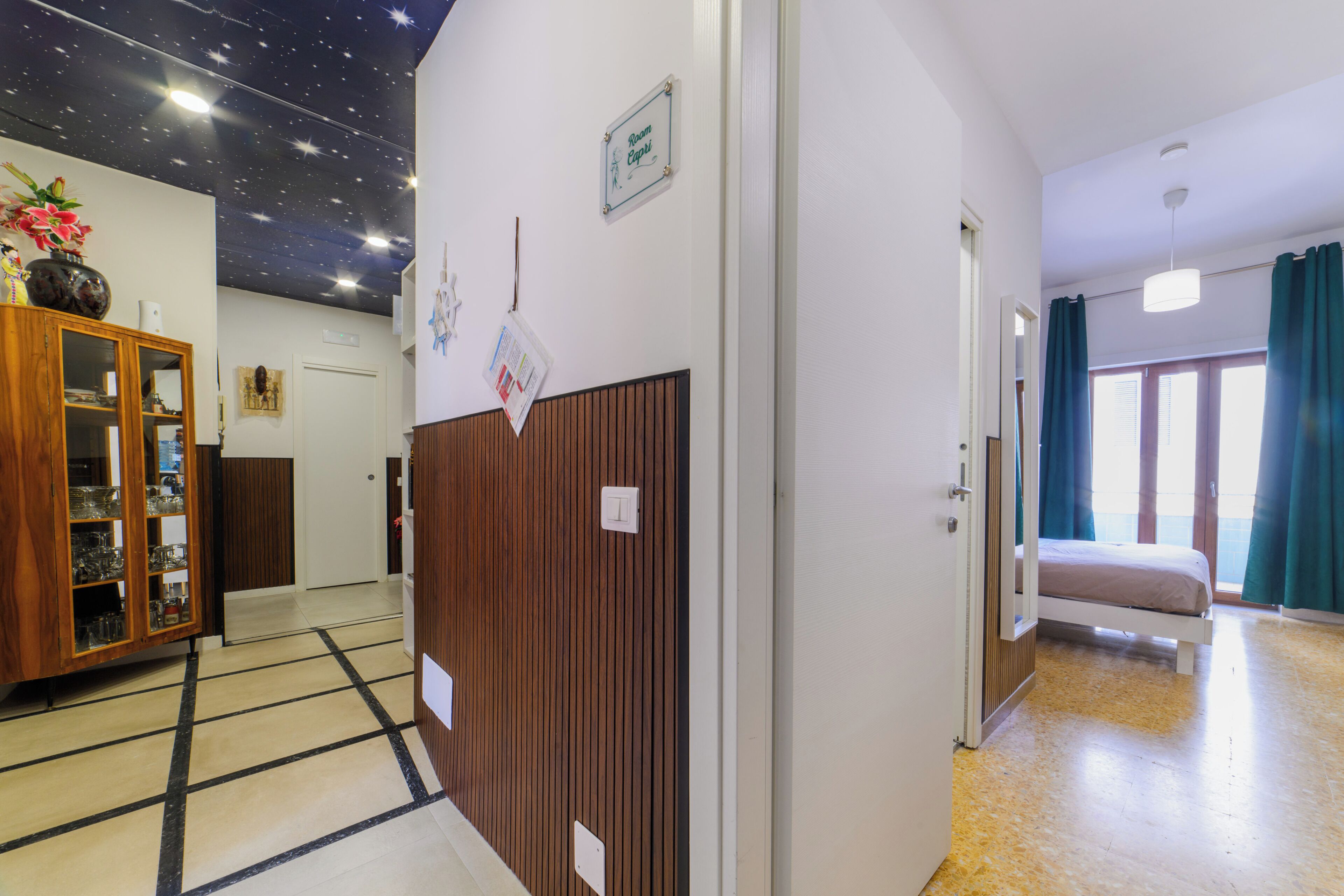 A hotel room with a bed, a wooden wardrobe, a starry ceiling, and a window with curtains.