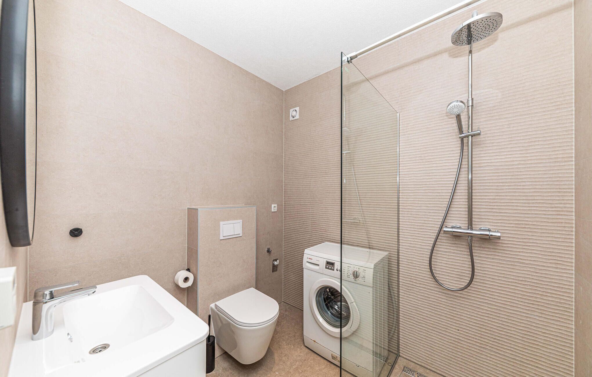 Un baño pequeño con ducha envuelta en vidrio, inodoro blanco y lavadora de carga frontal.