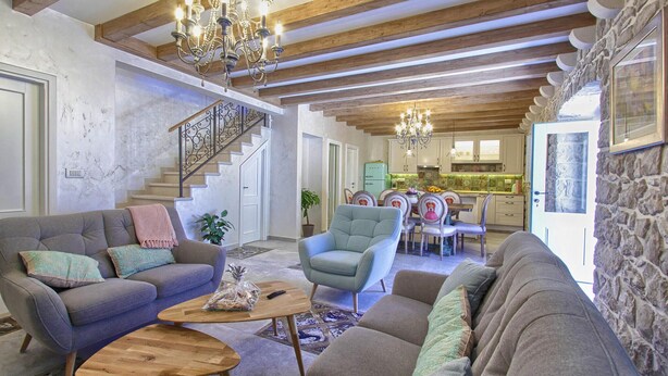 Un ampio soggiorno con soffitto alto, travi a vista in legno, una scala e una cucina sullo sfondo.