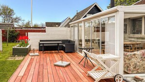 Een terras met buitenmeubilair, een glazen overkapping en een tuin.