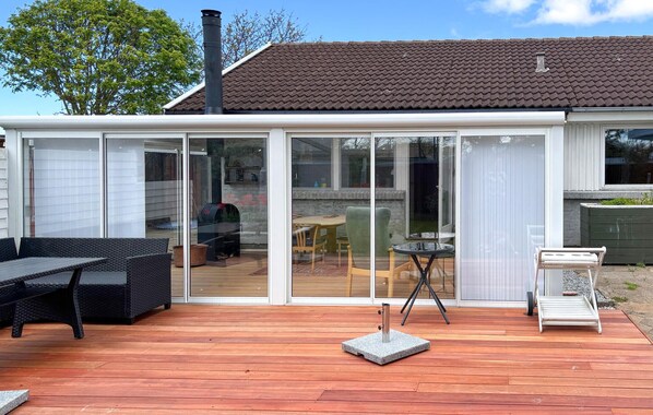 A covered patio with a wooden deck, a grill, and outdoor furniture.
