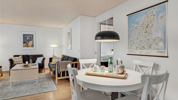 Een moderne woonkamer met een witte bank, een salontafel en een eethoek met een witte tafel en stoelen. Op de muur hangt een kaart van Nordjylland.