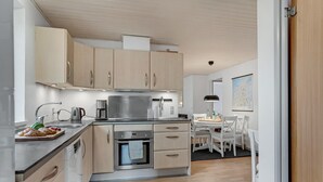 Een moderne keuken met lichte houten kastjes, roestvrijstalen apparatuur en een eethoek met witte stoelen.