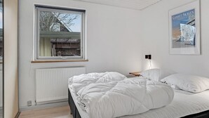 Een slaapkamer met een groot raam, een bed met wit beddengoed, een radiator en een poster aan de muur.
