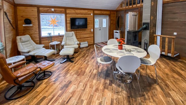 A cozy cabin interior with wooden walls, a dining area with a round table and chairs, a TV mounted on the wall, and a fireplace. - Nice home in Kåphult with kitchen (Kåphult)