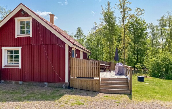 En rød træhytte med en træterrasse og et overdækket picnicbord.