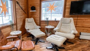 A room with wooden walls, two white cushioned chairs, a small round table, a brown leather chair, and a television mounted on the wall. - Nice home in Kåphult with kitchen (Kåphult)