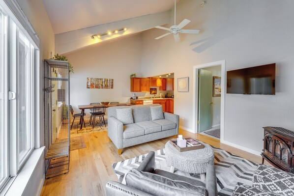Un salon spacieux avec un canapé gris, un tapis à motifs et un ventilateur de plafond.