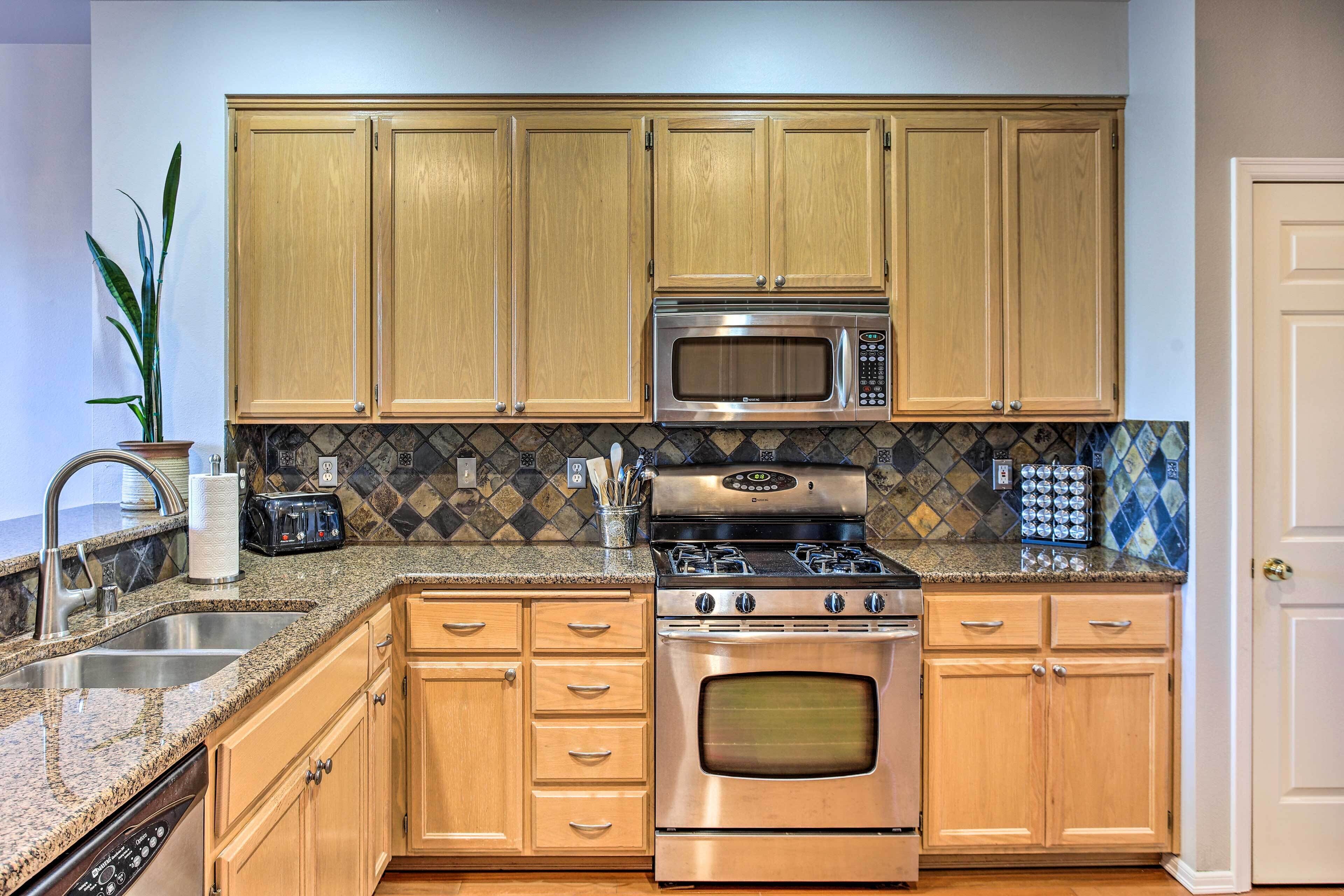 A kitchen with wooden cabinets, stainless steel appliances, a granite countertop, and a tiled backsplash.