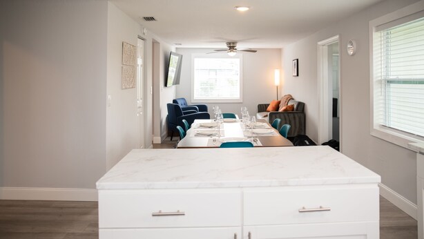 A modern kitchen with white cabinets, a marble countertop, and a dining area with blue chairs and a white table set for six.