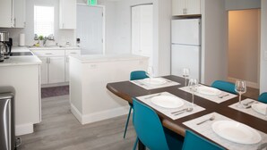 A modern kitchen with white cabinets, a built-in refrigerator, and a dining area with a wooden table set for four.
