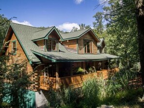 Una cabana de fusta amb un porxo i un teulat amb pendent pronunciat, envoltada per un bosc dens.
