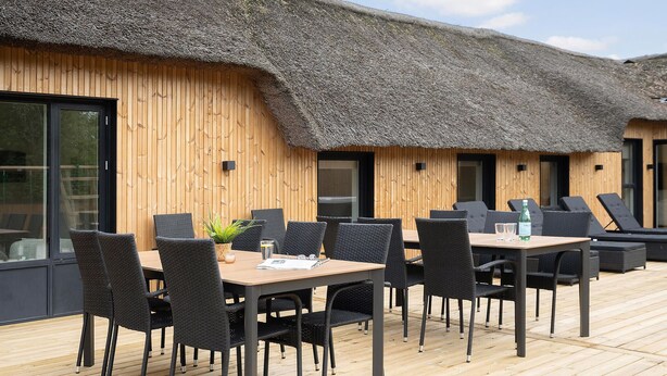 Eine Holzterrasse mit einem Reetdach, Sitzgelegenheiten und einem Tisch mit Stühlen.