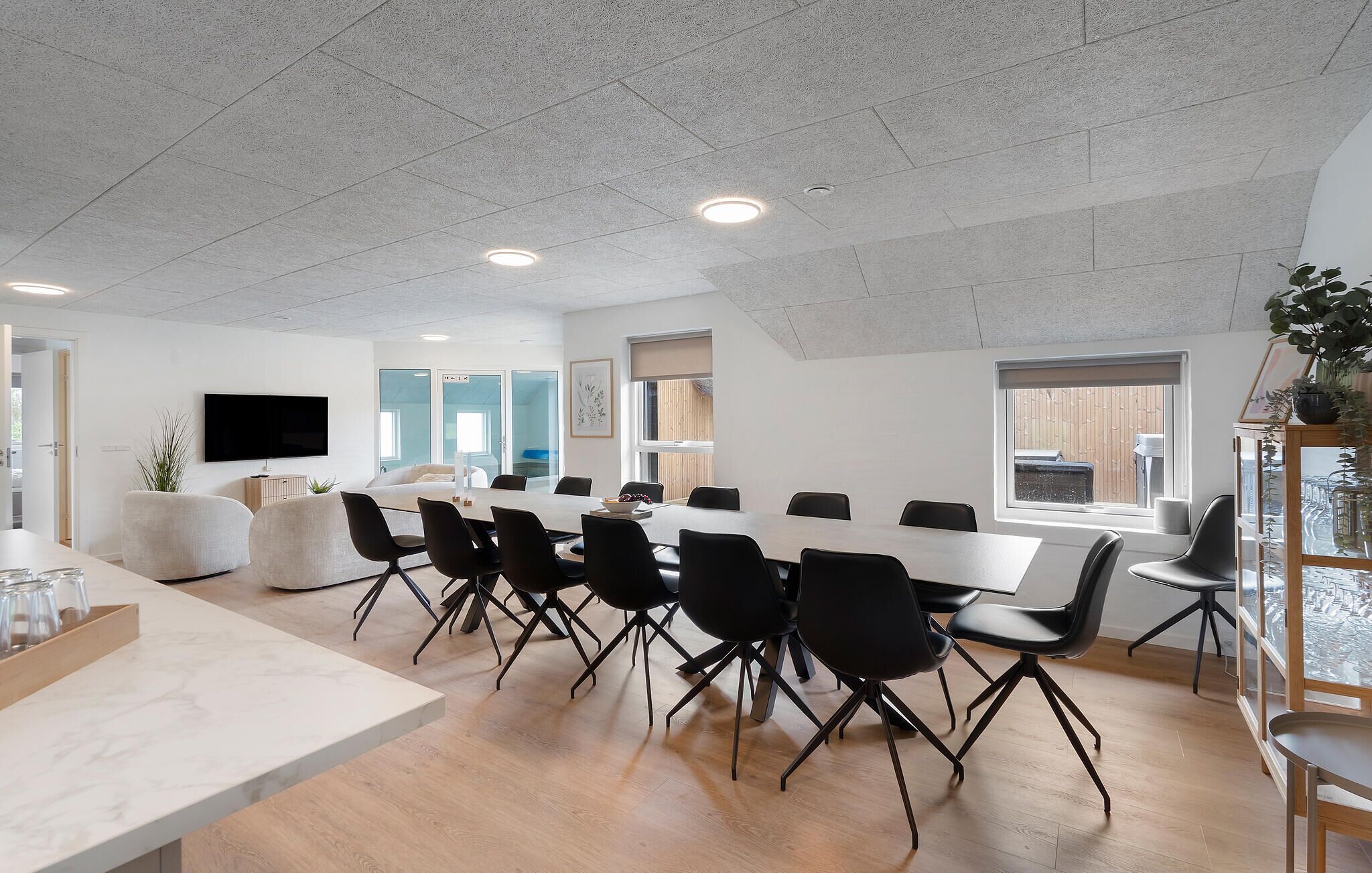 A conference room with a long table, black chairs, a TV, and a plant.